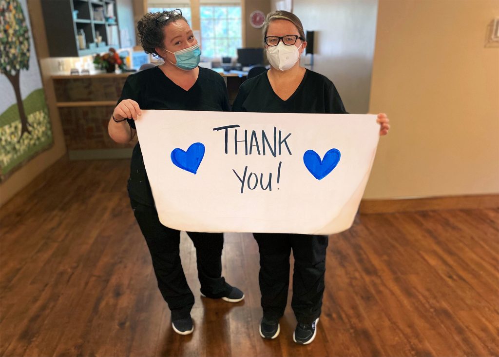 Two hospice nurses holding a thank you banner